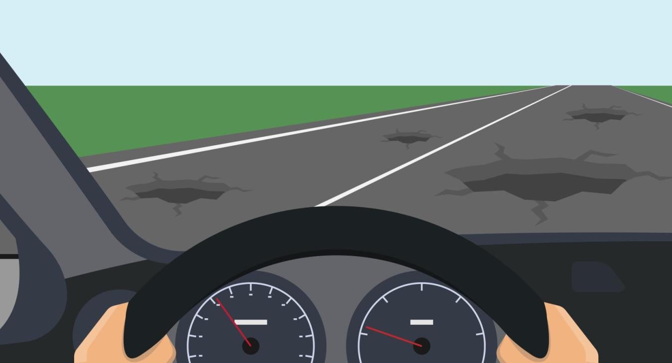 A driver looks out onto a road of potholes