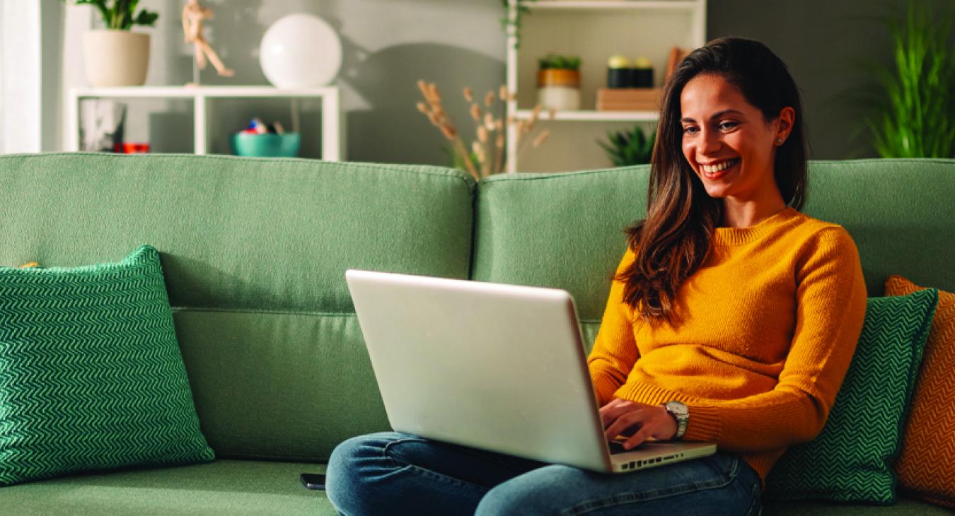 woman happily uses her laptop at home on her couch