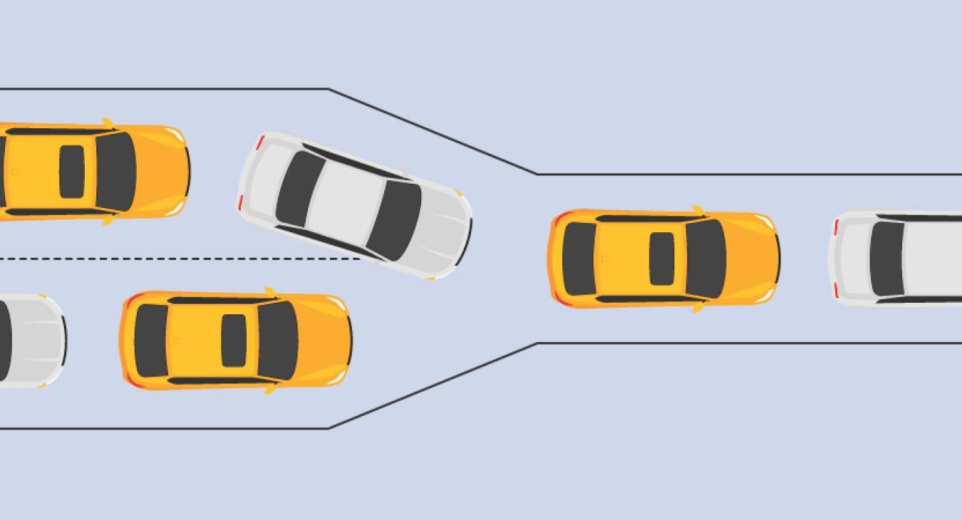 Cars on a two lane road slowly merge onto a one lane road